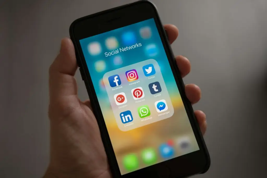 Person Holding Iphone Showing Social Networks Folder, uticaj mobilnih telefona na zdravlje