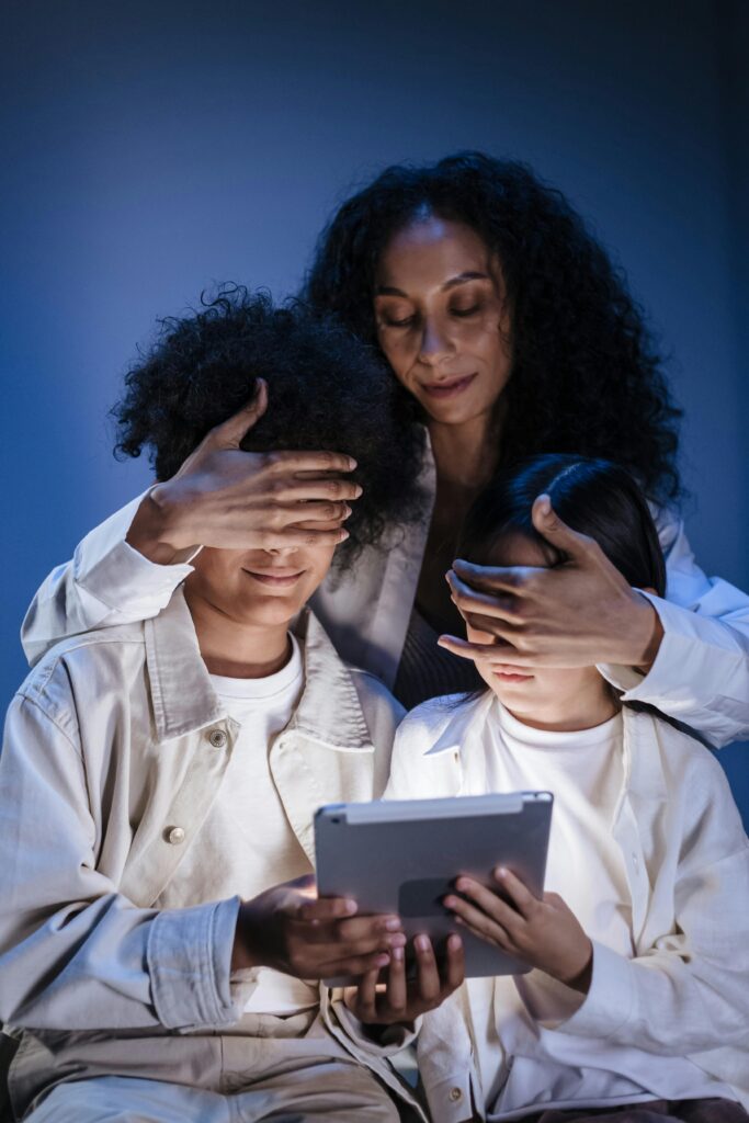 Mother covering eyes of her children with hands against internet content on digital pad, digitalna pismenost